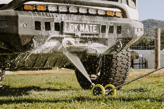 Truck with a sprayer attached to the back, spraying water on grass.