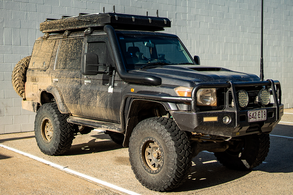 Dirt-covered off-road vehicle parked in a lot against a gray brick wall