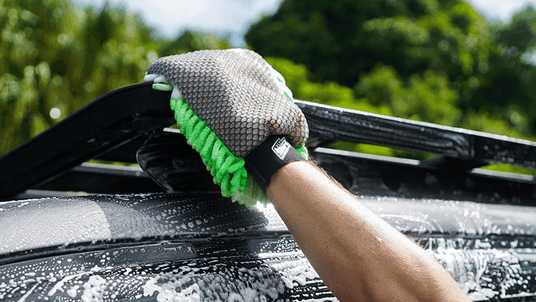 A hand using the Salt Shift 2-in-1 Wash Mitt to clean the top of a soapy vehicle. The mitt's dual-sided design is visible with the green microfiber strands in action.
