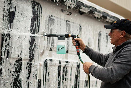 Person using a pressure washer to clean a wall with graffiti.