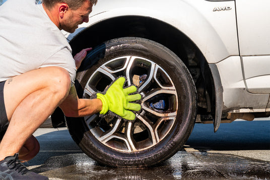 Person cleaning a car tire with a brush and green gloves