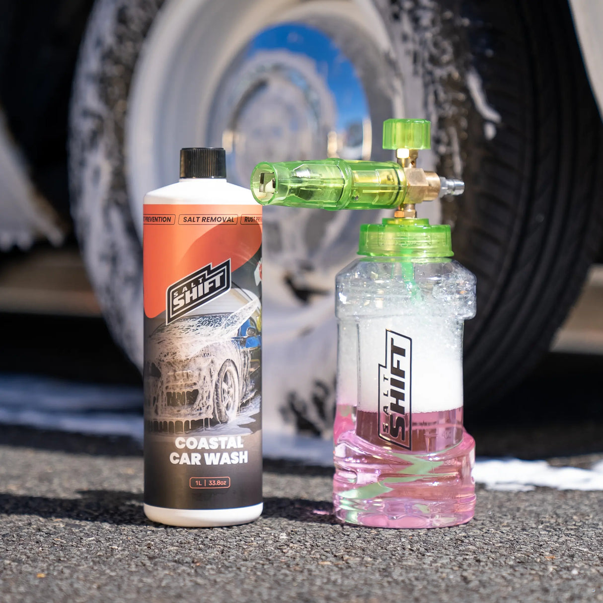 Two bottles of car wash products on a concrete surface with a car tire in the background.