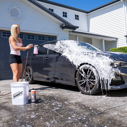 Woman washing a black car with soap suds in a driveway.