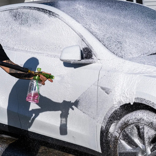 Person washing a white car with a bottle of cleaning solution