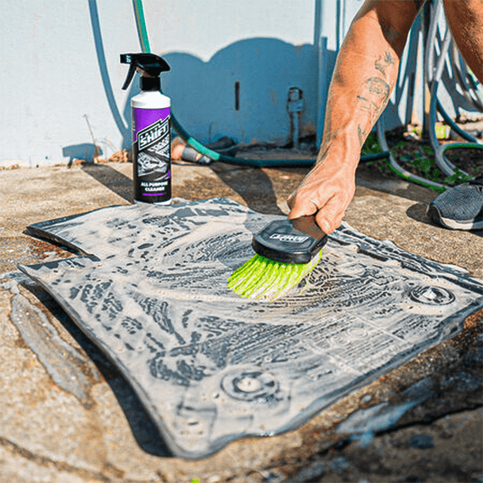 Person cleaning a metal surface with a brush and a bottle of cleaning solution.