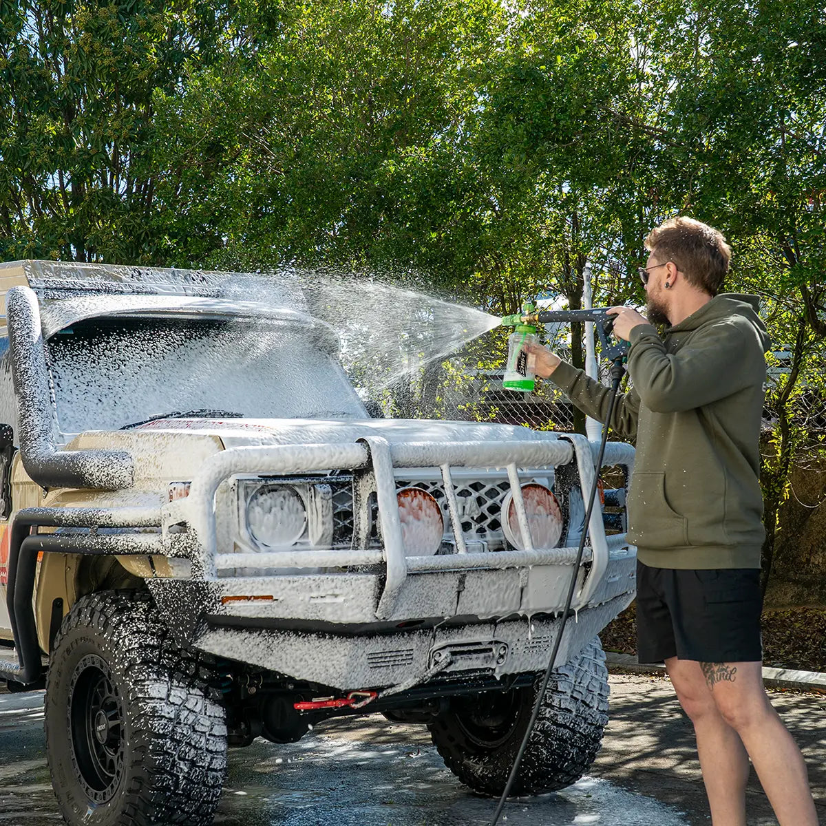 Person washing a large off-road vehicle with a hose outdoors.