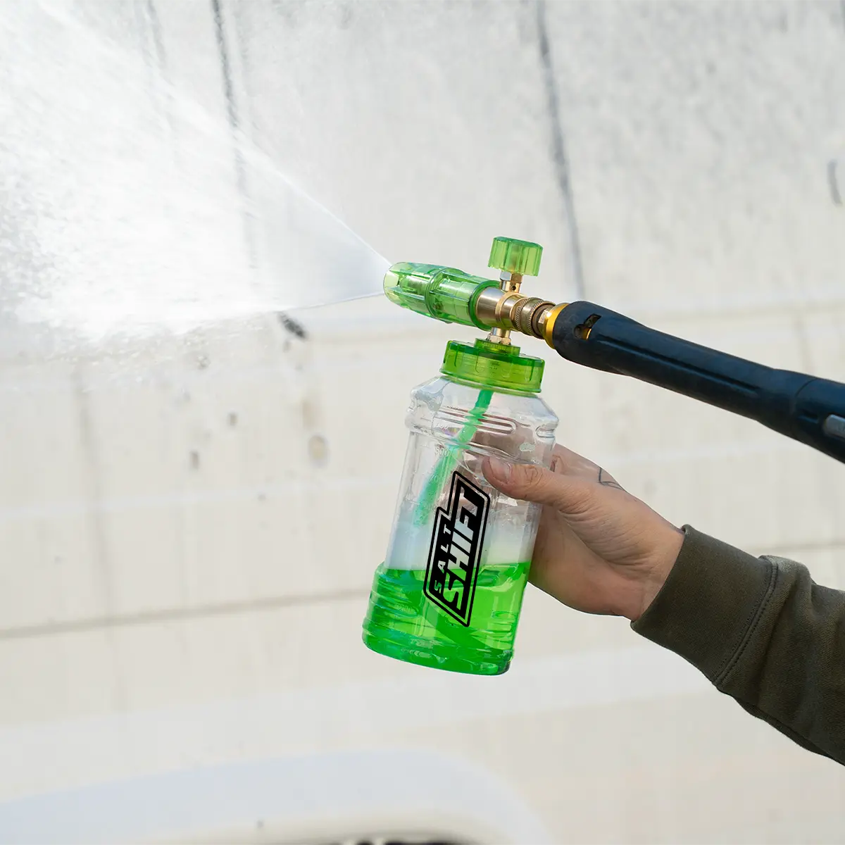 Person holding a green spray bottle with a nozzle attached, against a white background