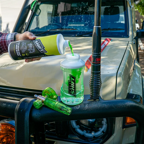 Person pouring a green liquid from a bottle into a plastic container on a vehicle's front bumper.