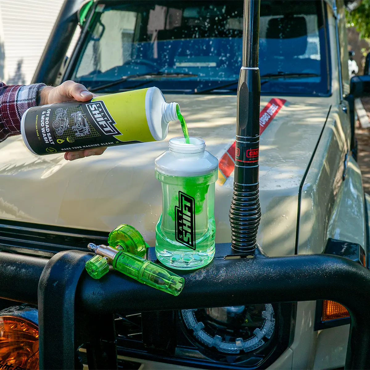 Person pouring a green liquid from a bottle into a plastic container on a vehicle's front bumper.