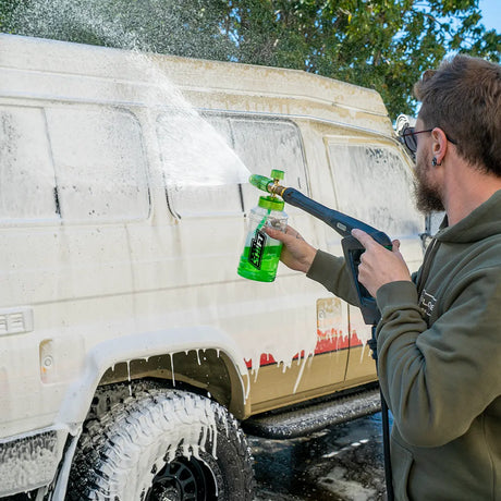 Person washing a van with a high-pressure washer and cleaning solution bottle.
