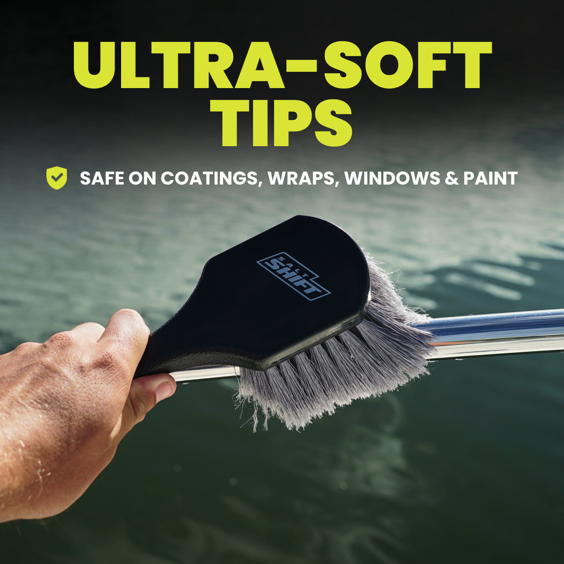 Hand holding a cleaning brush with ultra-soft tips, safe on coatings, wraps, windows, and paint, against a blurred water background.