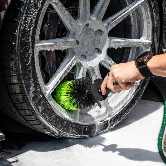 Person cleaning a car wheel with a brush