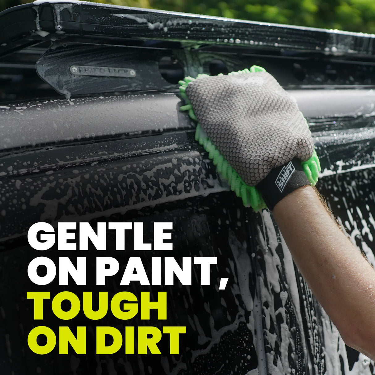 Person cleaning a car with a soapy sponge, wearing a green and gray glove.
