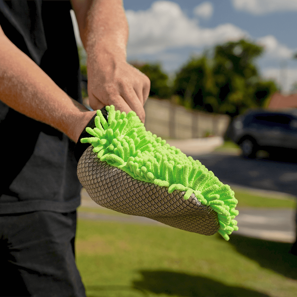 A person putting on the Salt Shift 2-in-1 Wash Mitt outdoors. The mitt has a textured grip on one side and soft green microfiber strands on the other.