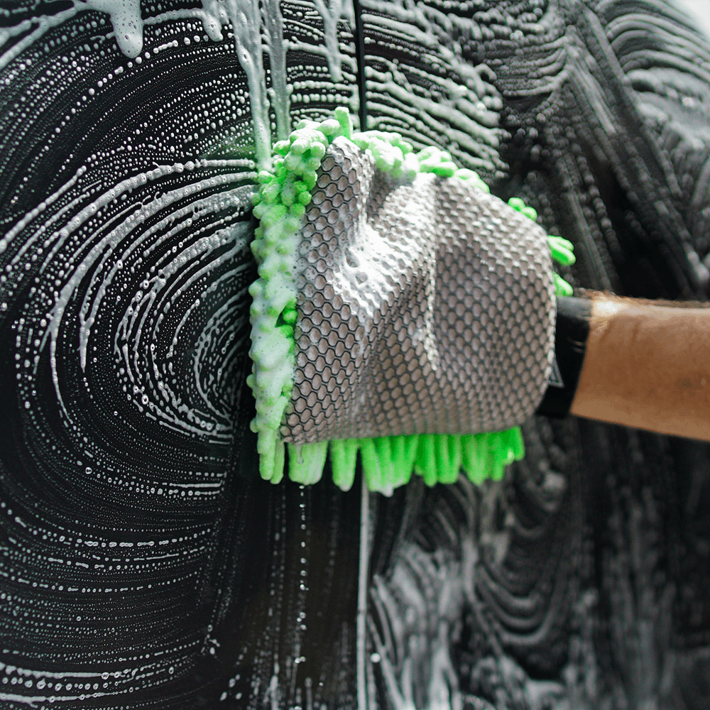 The Salt Shift 2-in-1 Wash Mitt creating swirling soap patterns on a black vehicle. The mitt’s green microfiber side is covered in foam.