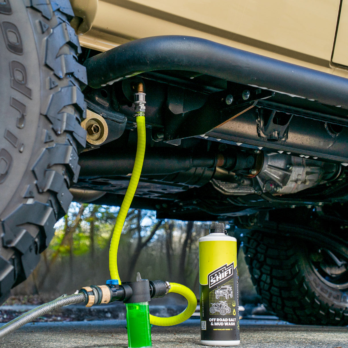 Close-up of a vehicle's undercarriage with a yellow hose and canister, likely for lubrication or maintenance.