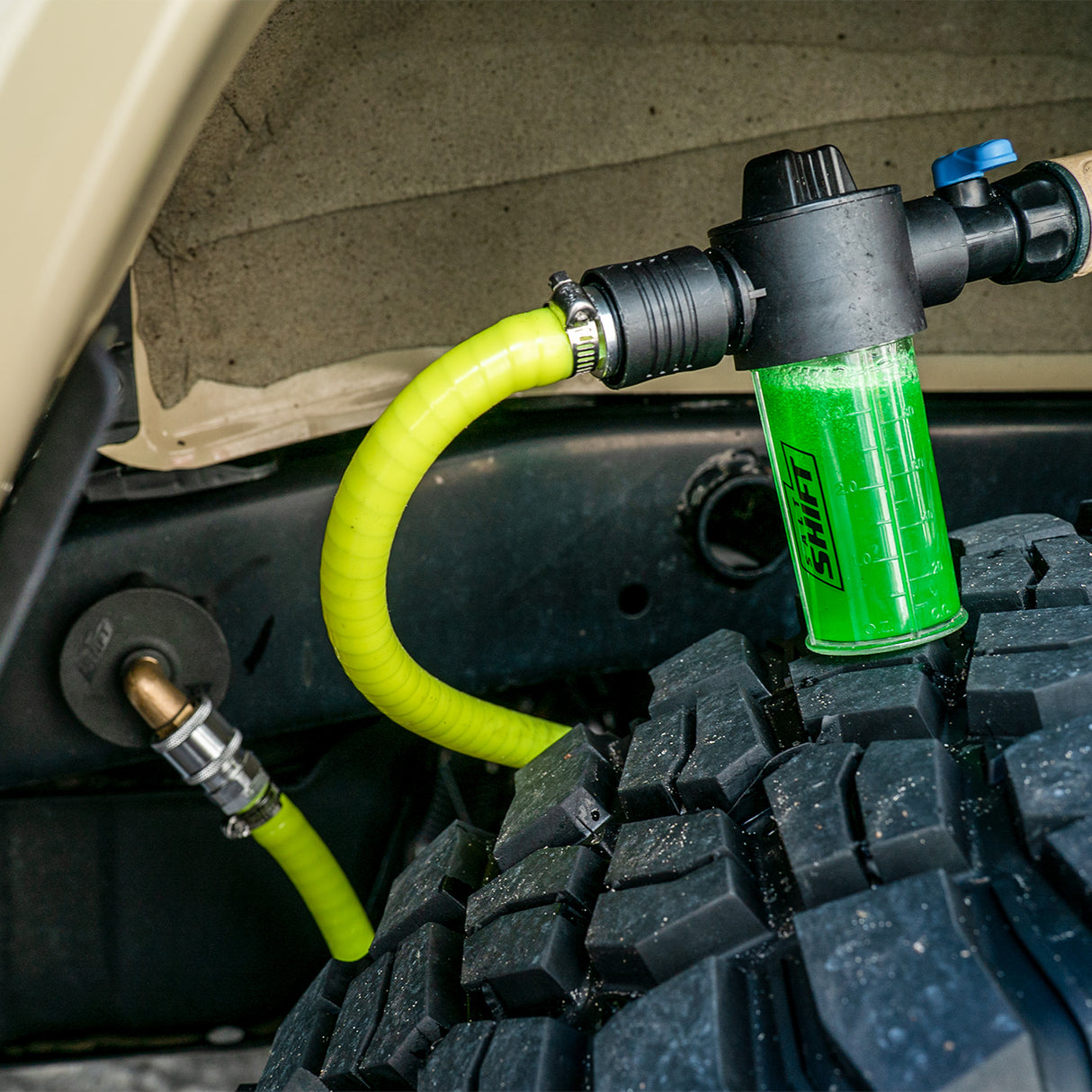 Green fluid filter with yellow hose attached to a vehicle's engine bay.