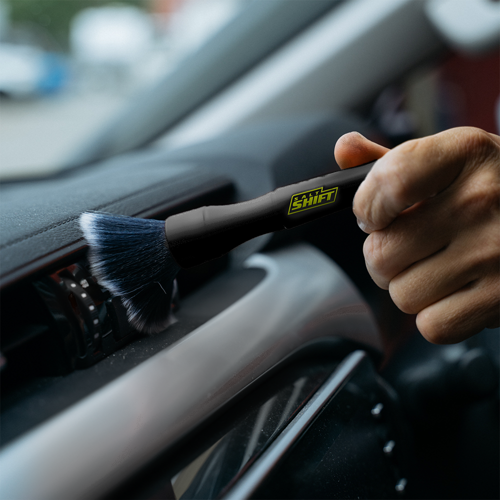 A person uses a Salt Shift detailing brush to clean a car's air vents.