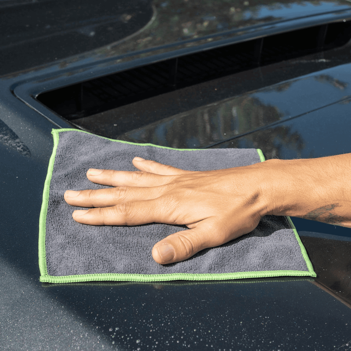 A man holding a black and green microfibre cloth, polishing car surface.