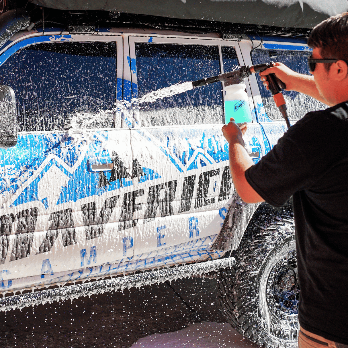 A person uses a Salt Shift foam cannon to spray a 4WD with cleaning foam.