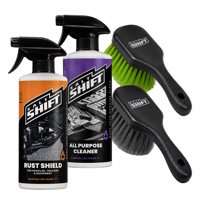 Two Salt Shift branded spray bottles and two cleaning brushes on a plain white background. One bottle has an orange-to-brown gradient label reading Rust Shield, and the other has a purple-to-black label reading All Purpose Cleaner.