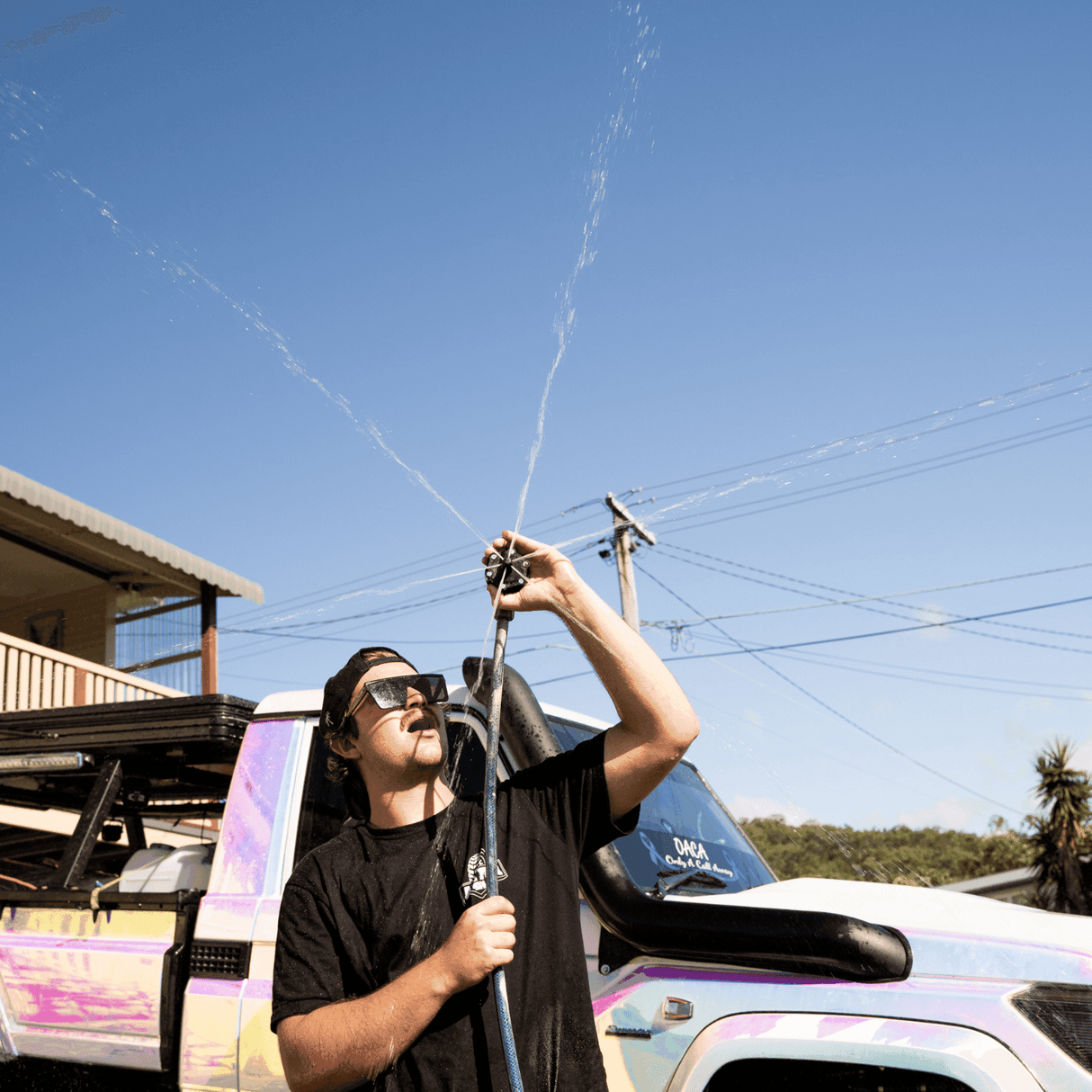 A person holds a Salt Shift chassis flusher spraying water in multiple directions.
