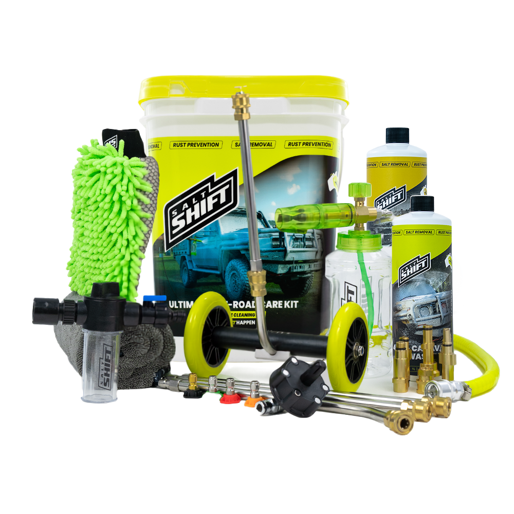 A comprehensive car care kit displayed on a clean white background, featuring a large white bucket with a bright yellow lid and label, a green microfiber wash mitt, brass nozzles and hoses, a pressure washer wand, a foam cannon, bottles of cleaning solutions, and a gray sponge.