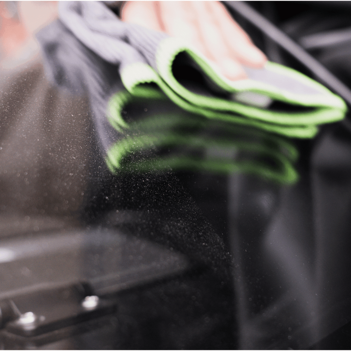Close-up of a microfiber cloth wiping a glossy black surface, removing dust and enhancing shine for a streak-free finish. Premium car detailing and surface cleaning.