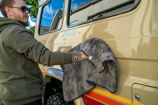 Man cleaning a beige vehicle with a gray towel outdoors