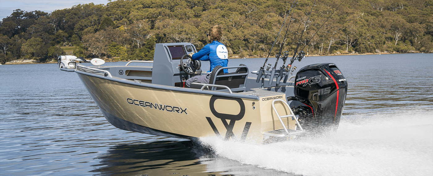 Person fishing from a boat branded 'OceanWorx' on a lake with trees in the background