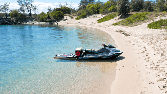 Jet ski on a sandy beach with clear water and greenery in the background