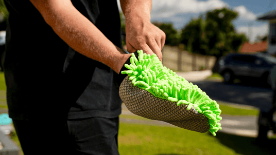 Person holding a green and black shoe brush outdoors