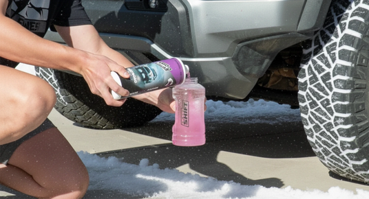 Person using a bottle to clean a car tire with snow on the ground