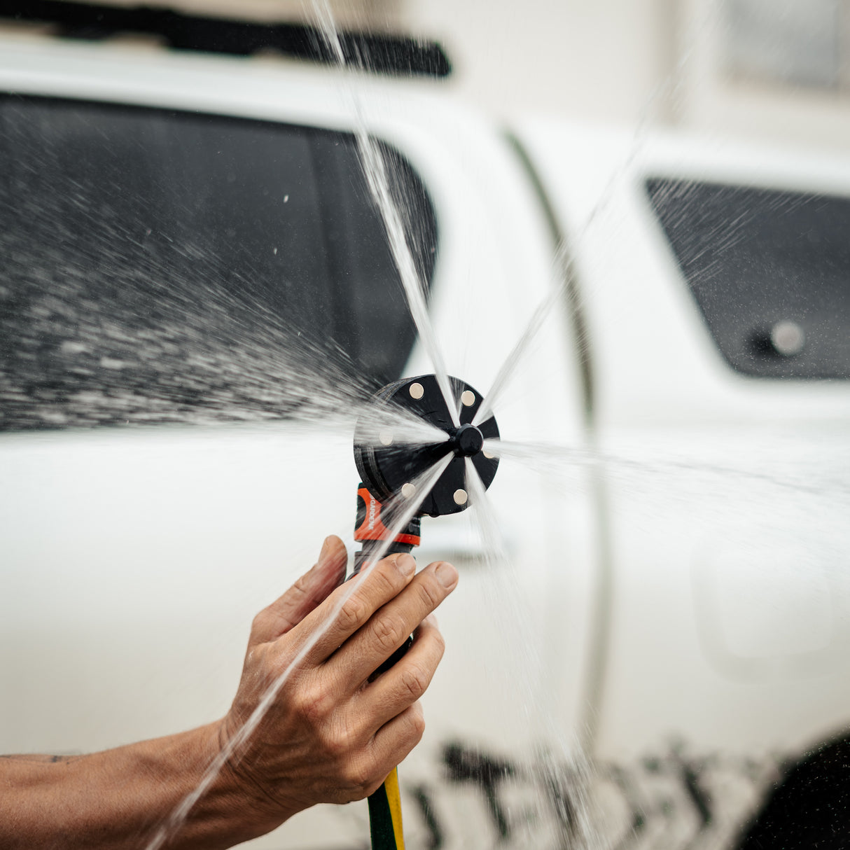 A person holds a Salt Shift chassis flusher spraying water in multiple directions.