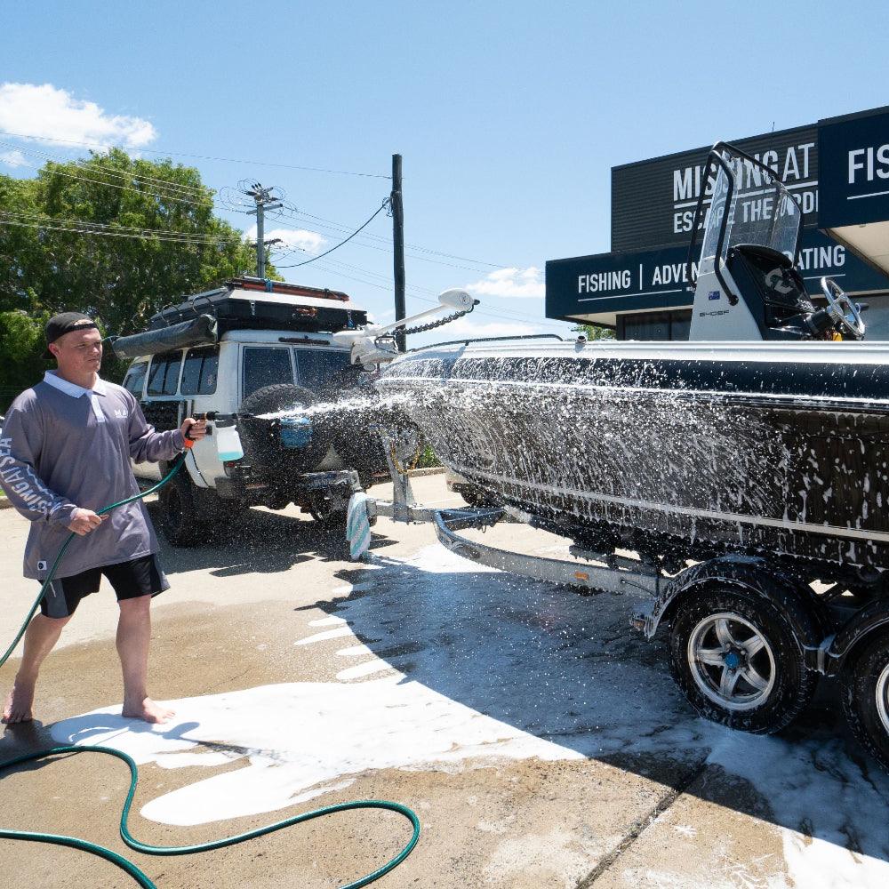A person uses a Salt Shift foam cannon to spray a boat with cleaning foam.