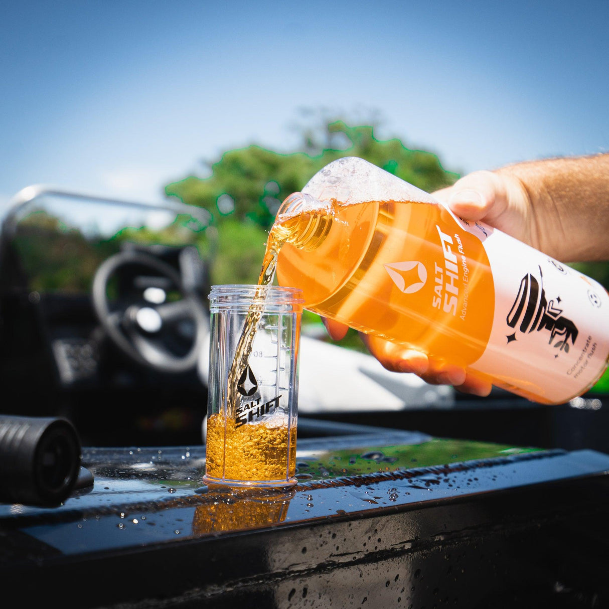 A person pours Salt Shift Wash into a branded bottle, with a marine vehicle in the background.