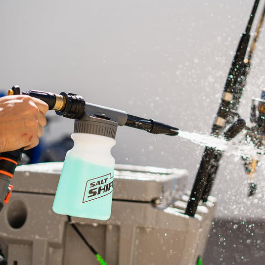 A person uses a Salt Shift foam cannon to spray a boat with cleaning foam.