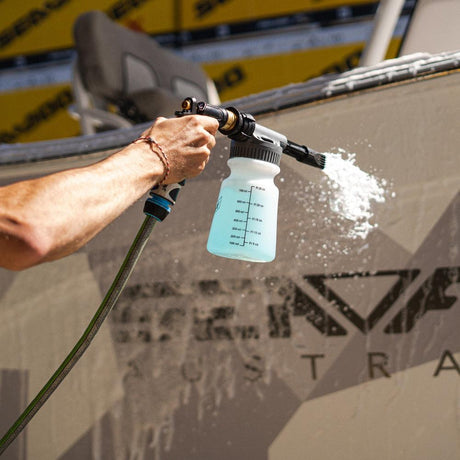 A person uses a Salt Shift foam cannon to spray a boat with cleaning foam.