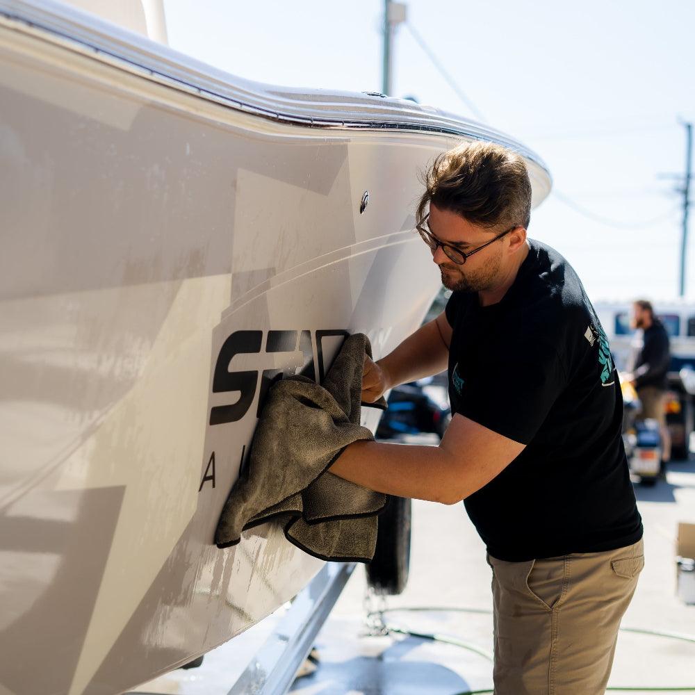 A person wipes down a boat with a grey microfibre towel, ensuring a clean and polished finish.