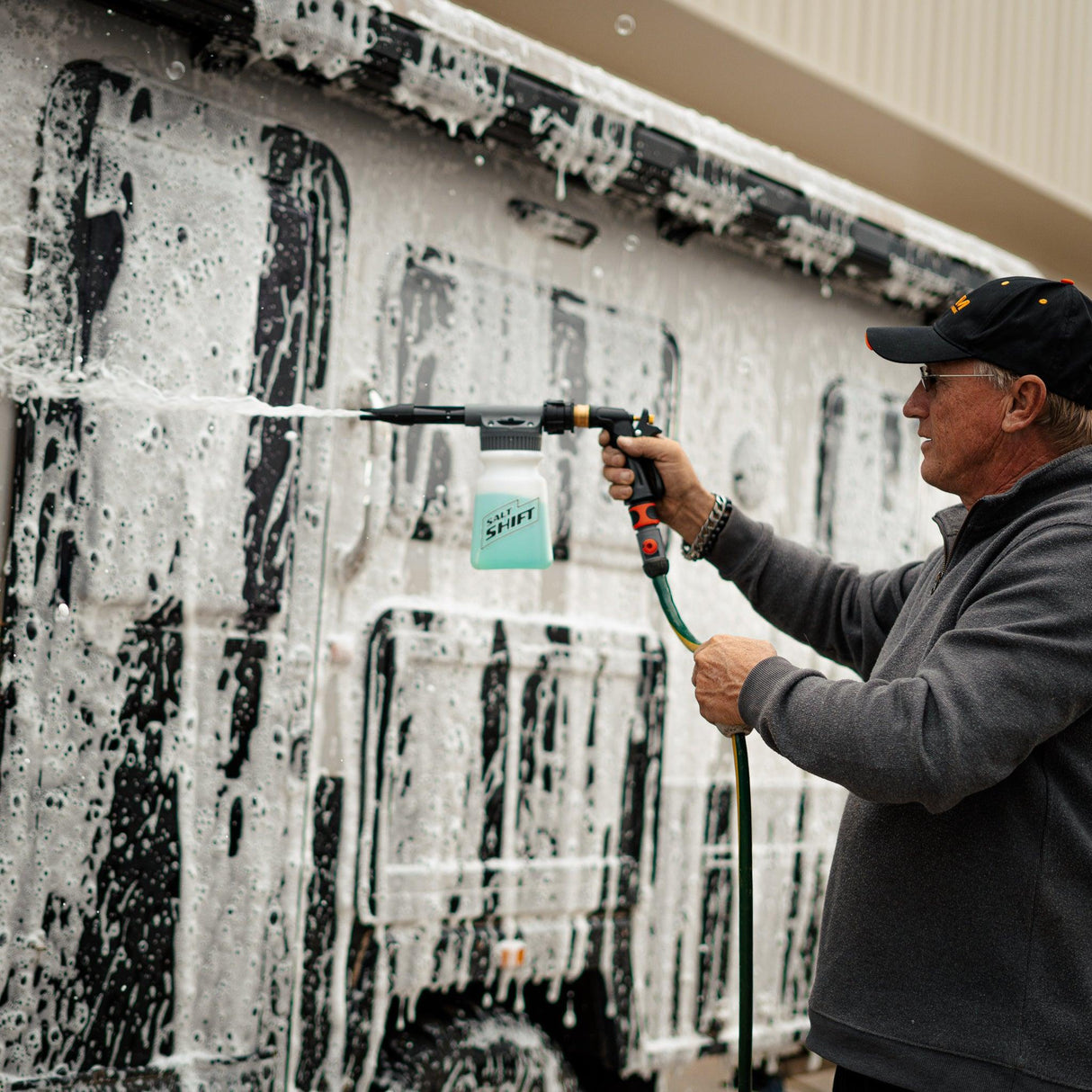 A person uses a Salt Shift foam cannon to spray a caravan with thick cleaning foam.