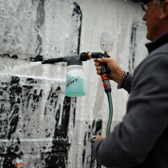 A person uses a Salt Shift foam cannon to spray a caravan with cleaning foam.