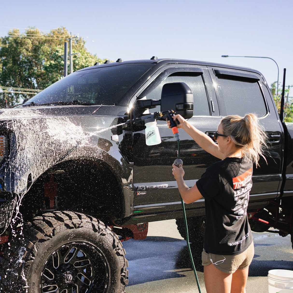 A person uses a Salt Shift foam cannon to spray a truck with cleaning foam.