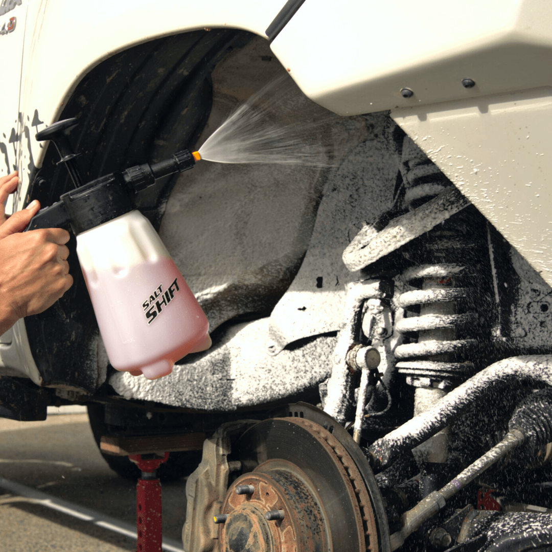 A person uses a Salt Shift foam sprayer to clean a 4x4 wheel well and suspension.