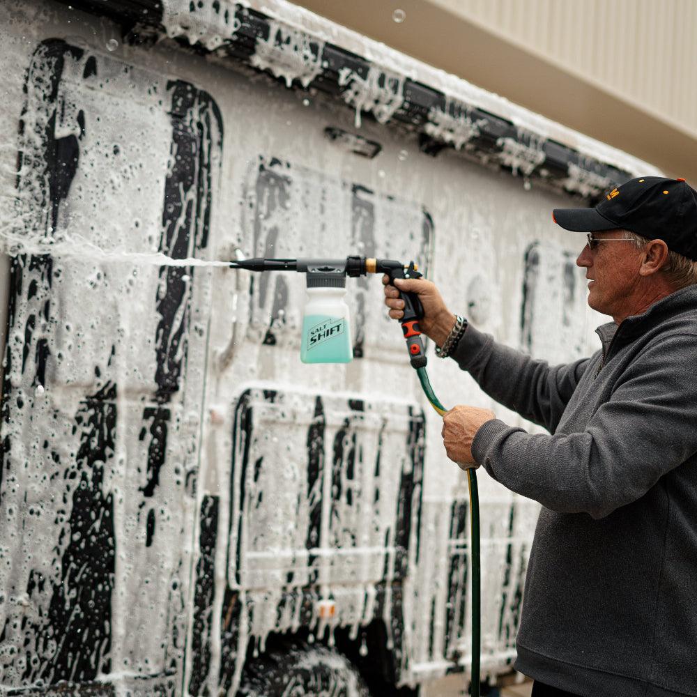 A person uses a Salt Shift foam cannon to spray a caravan with cleaning foam.