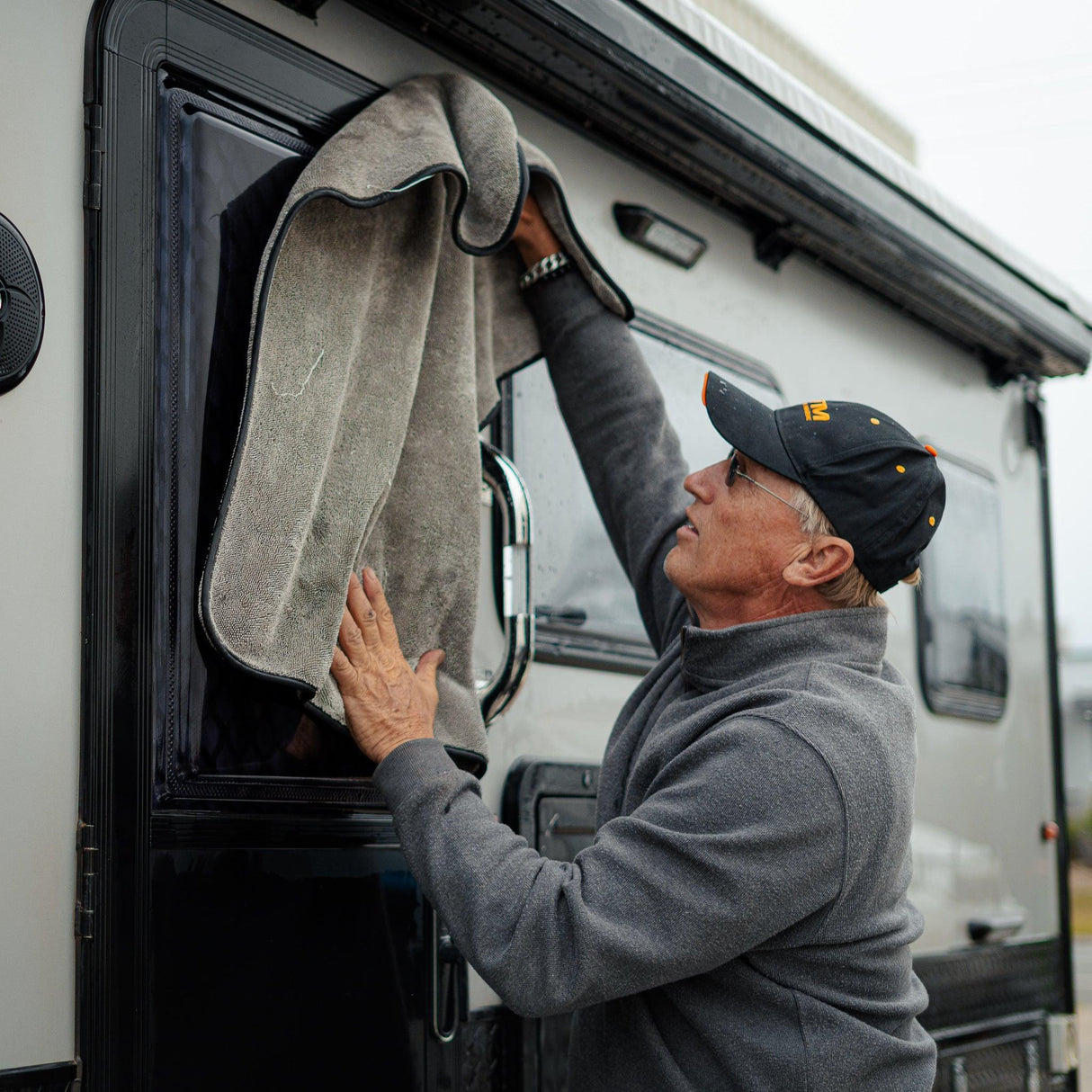 A person wipes down a caravan with a grey microfibre towel, ensuring a clean and polished finish.