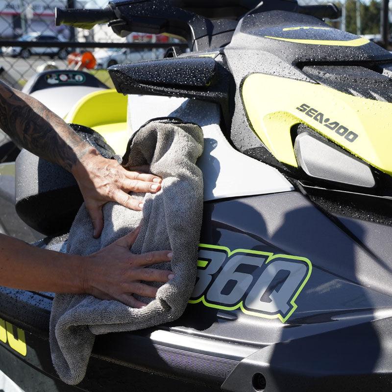 A person wipes down a jetski with a grey microfibre towel, ensuring a clean and polished finish.