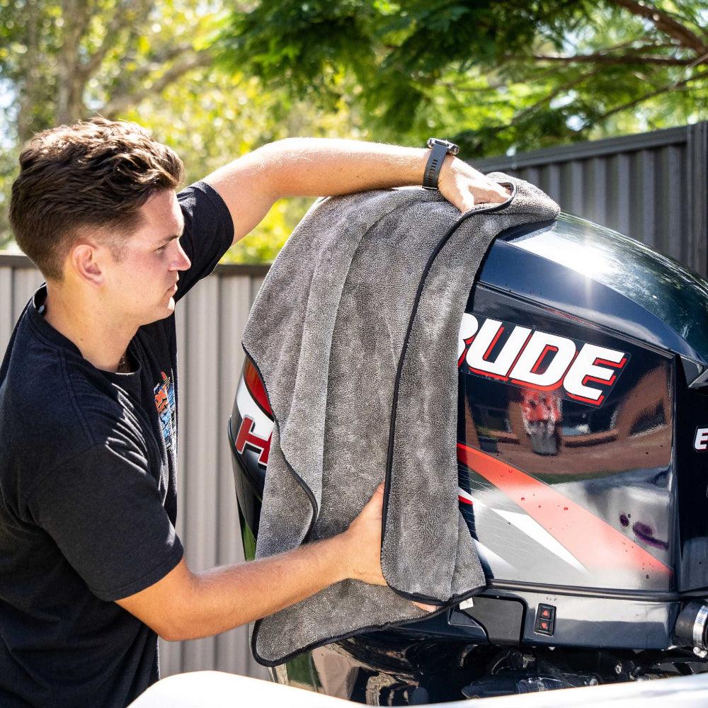 A person wipes down a boat engine with a grey microfibre towel, ensuring a clean and polished finish.