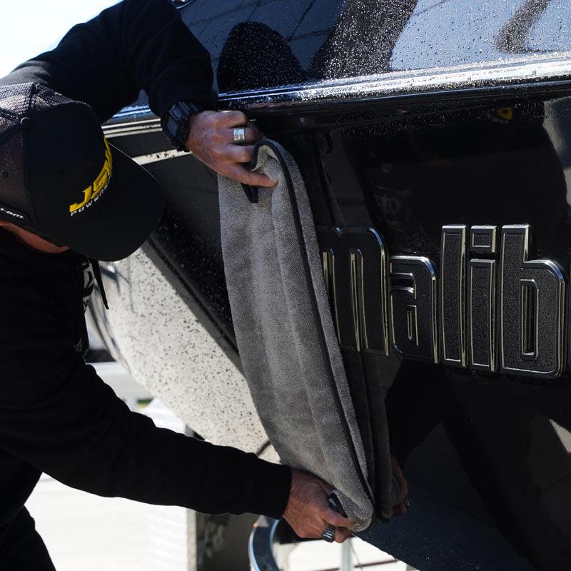 A person wipes down a boat with a grey microfibre towel, ensuring a clean and polished finish.