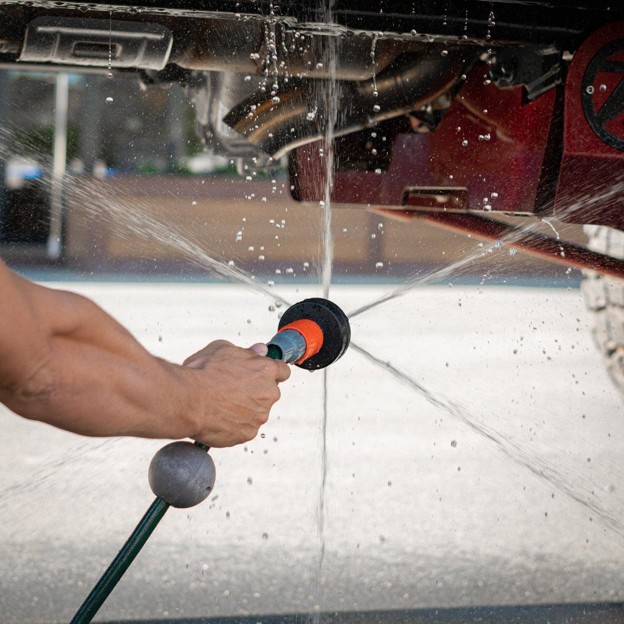 A person holds a Salt Shift chassis flusher spraying water in multiple directions on a car undercarriage