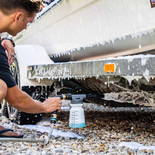 Man using a foam gun to wash a boat undercarriage with Salt Shift cleaning solution, removing salt and grime for corrosion protection.